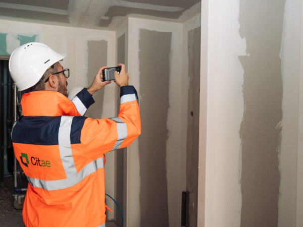 Un consultant Citae, vu de dos, photographie les cloisons d'un couloir en chantier