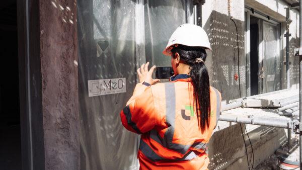 Une consultante Citae, vue de dos, photographie une façade en rénovation près d'un échafaudage